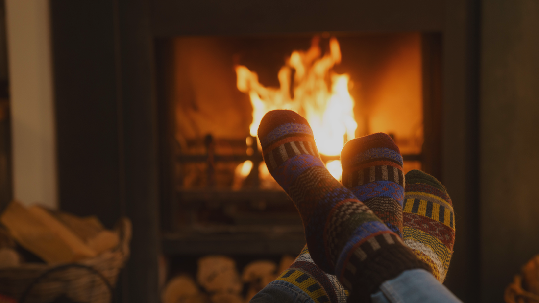 Homefire Cutting Heat Costs. Warm feet in front of a fire. Kiln-dried firewood logs in basket next to the fire.